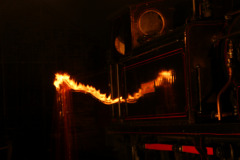 Long exposure shot of a man carrying a shovel of lit coal at night.